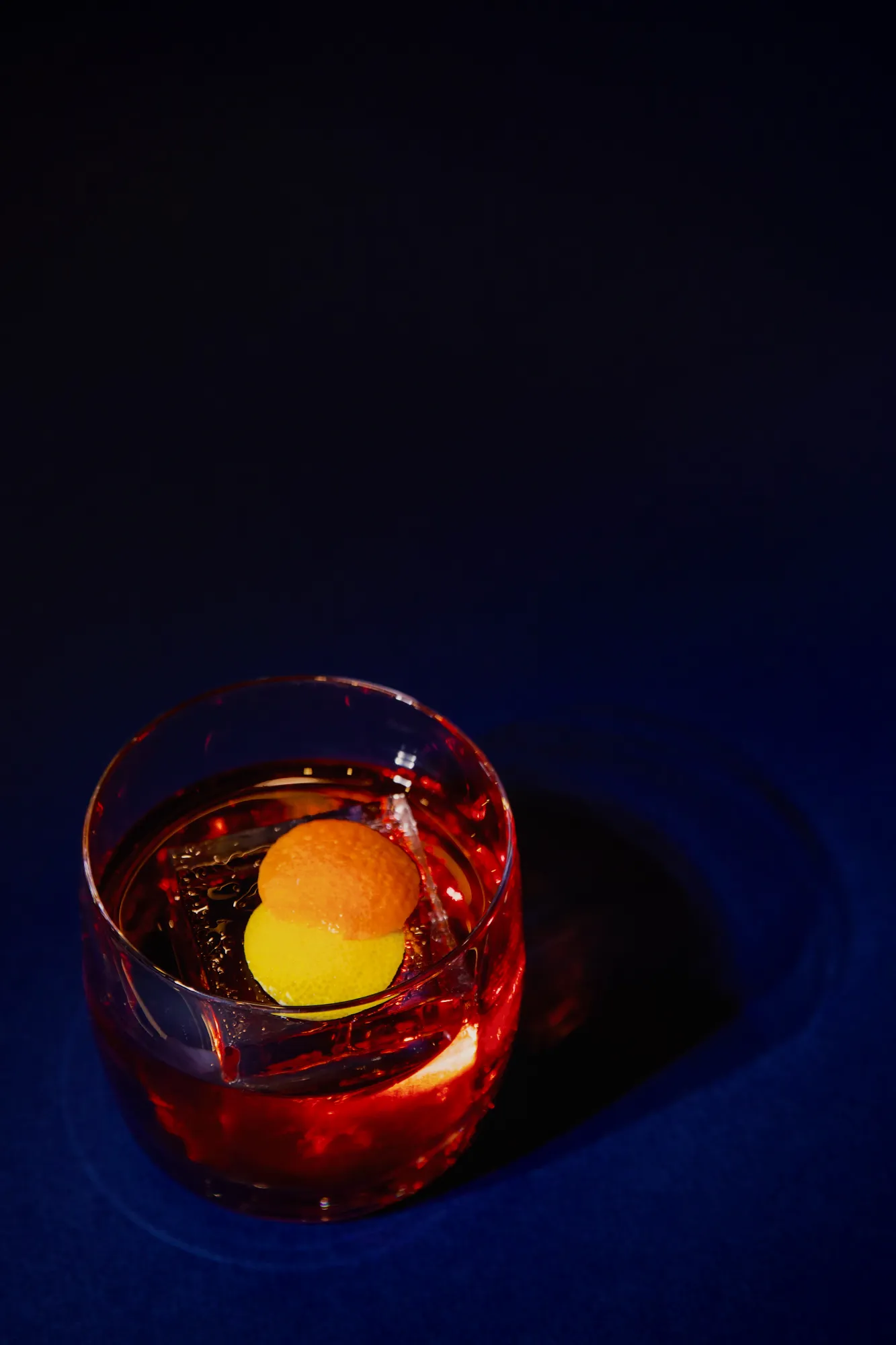 A deep red cocktail in a rocks glass, garnished with orange peel on the ice