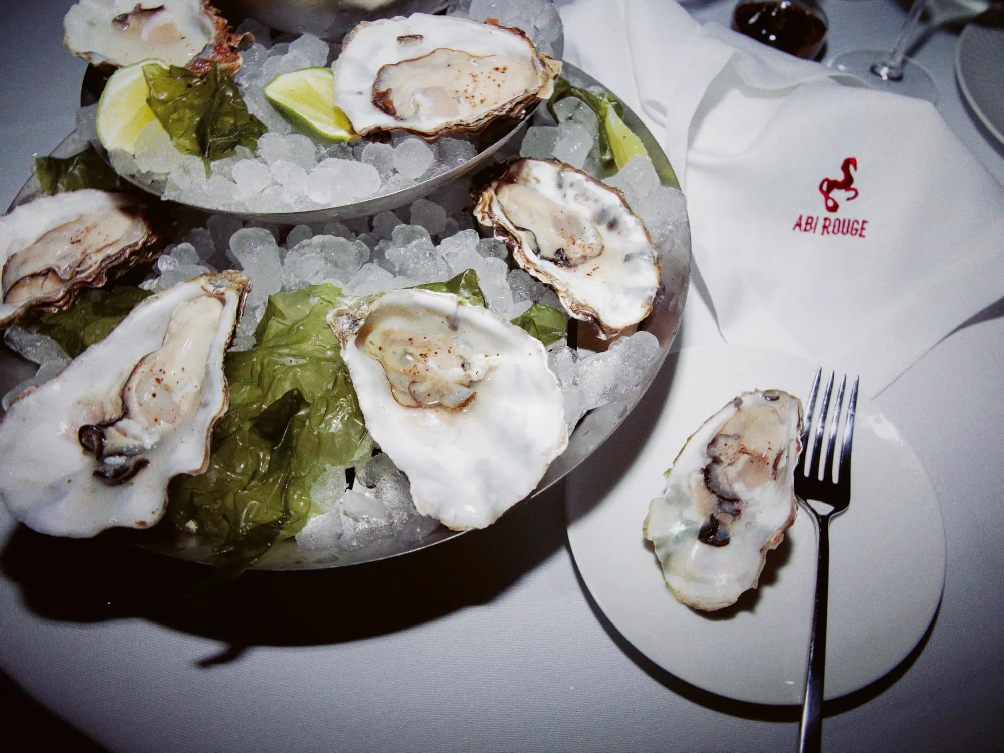 Oysters on crushed ice with lemon, beside a napkin embroidered with the Abi Rouge horse