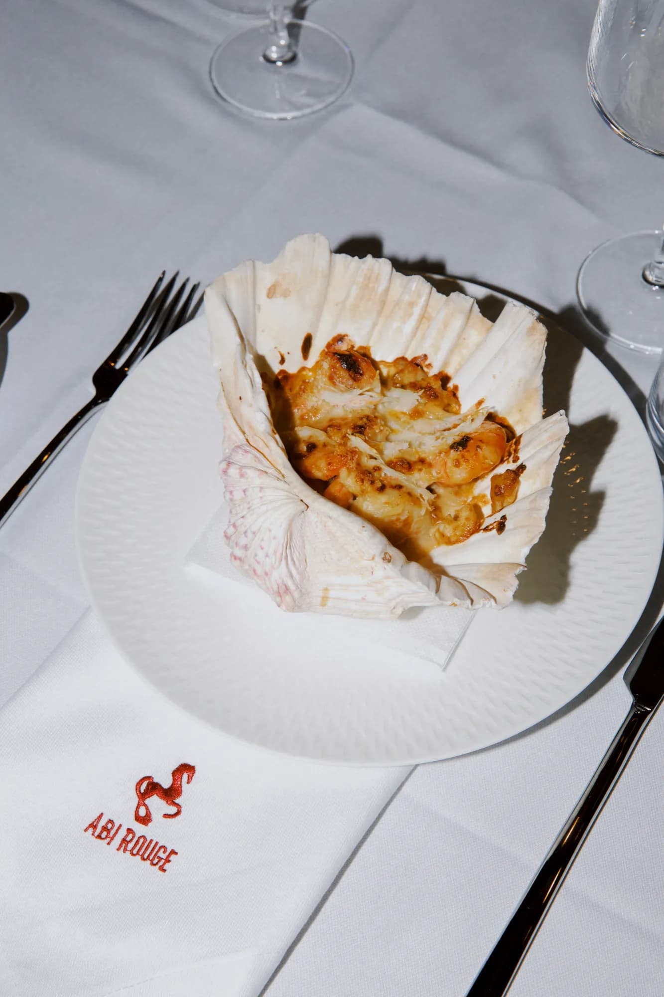 Baked shellfish in the shell on a white plate, with the Abi Rouge napkin beside it