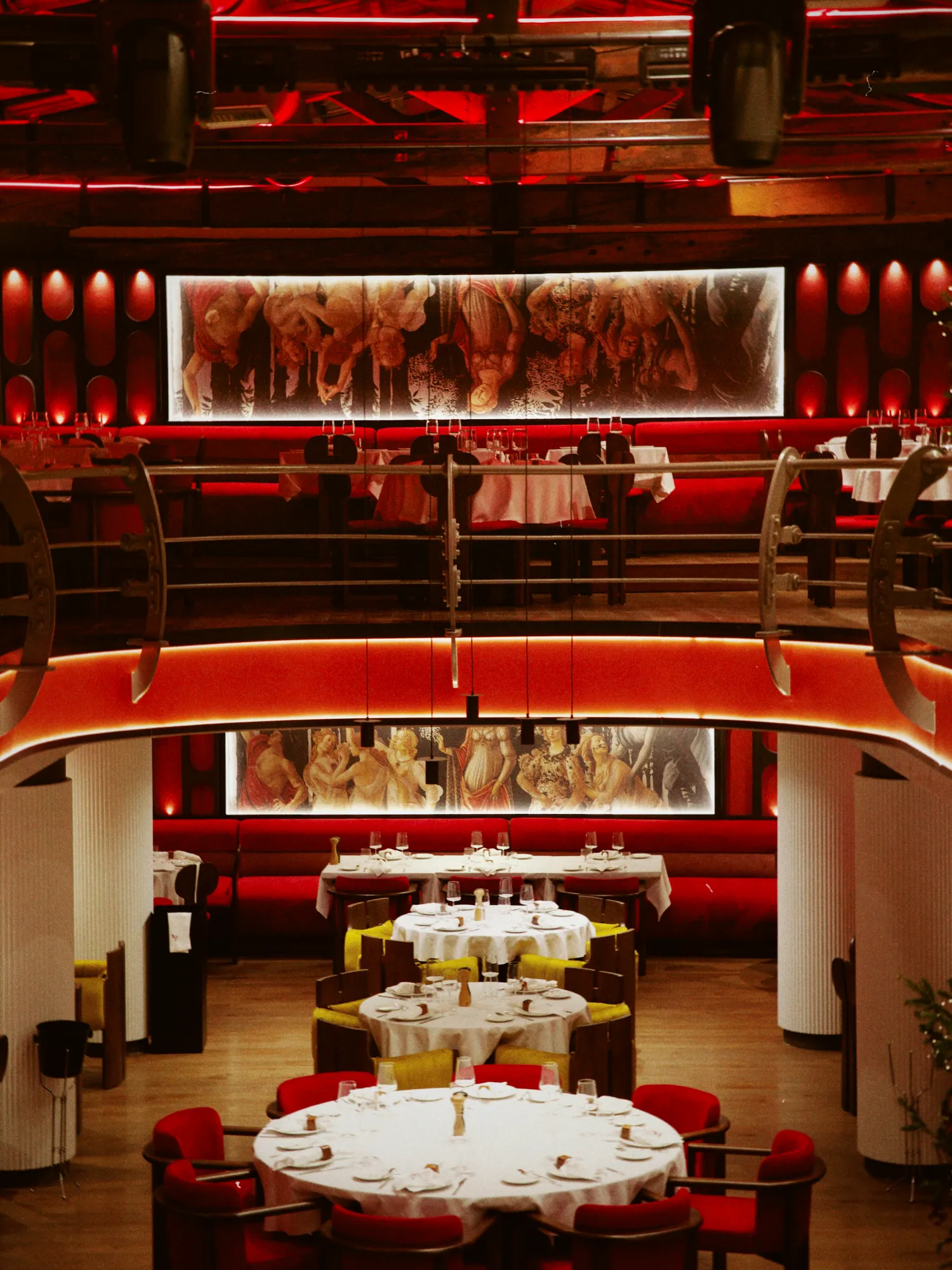 The two-level dining room at Abi Rouge, in red light, with set tables and a tapestry on each floor