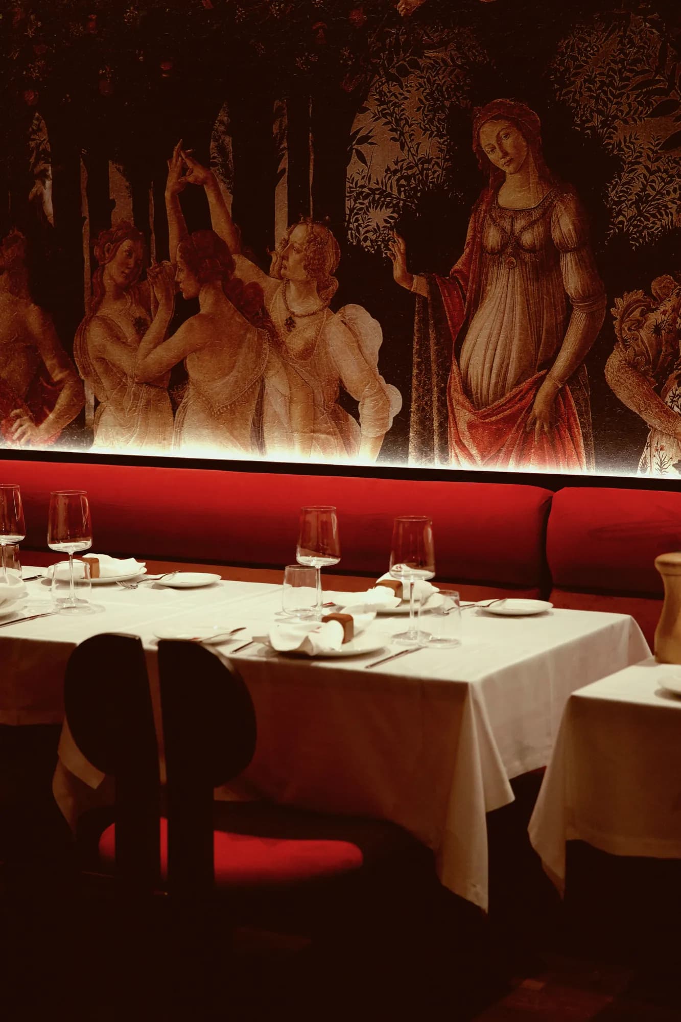 A long table beneath a tapestry of figures, with red banquettes and wine glasses