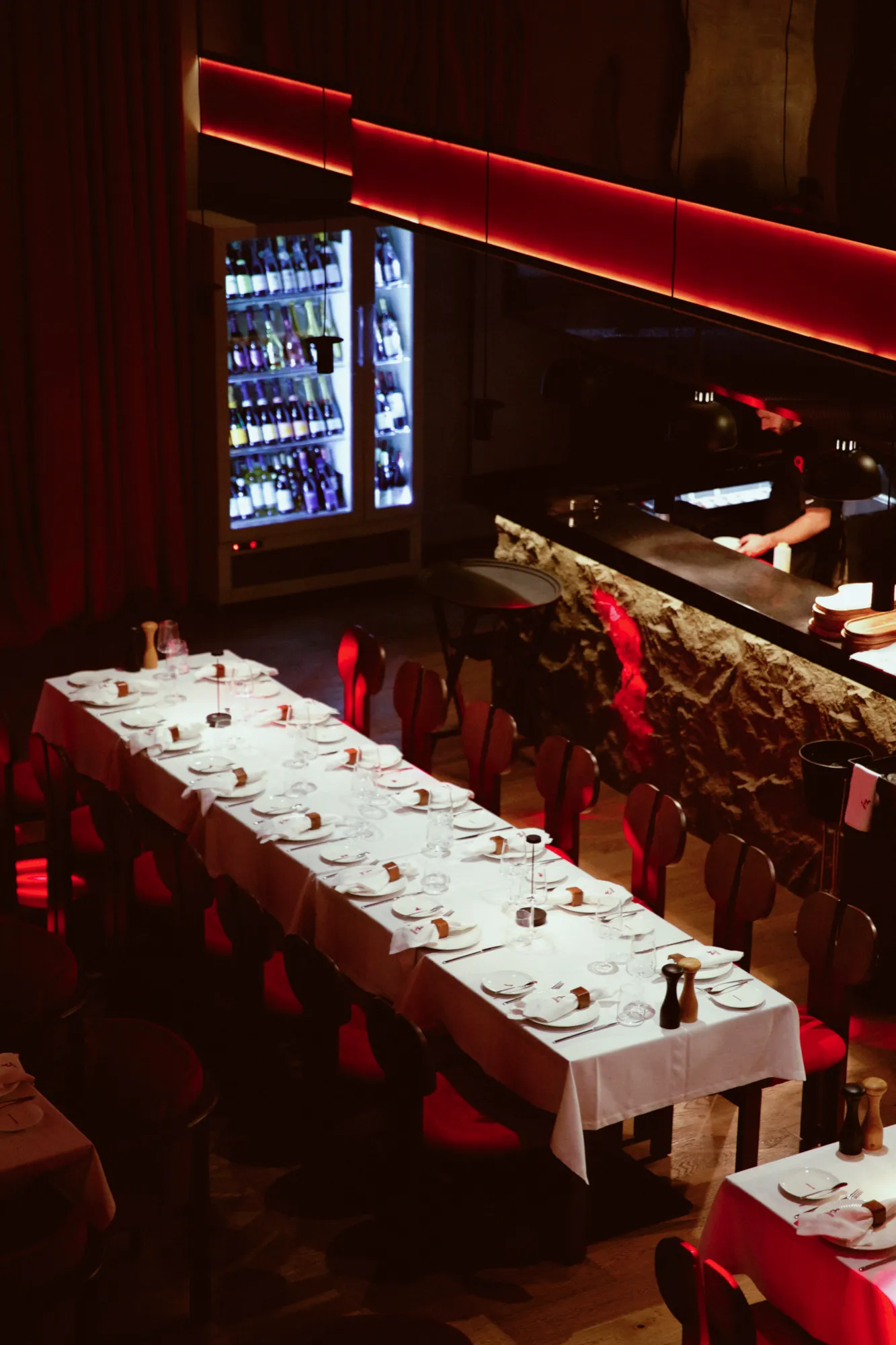 A long table set for a private dinner beside the pass, with a wine fridge and the kitchen counter behind it
